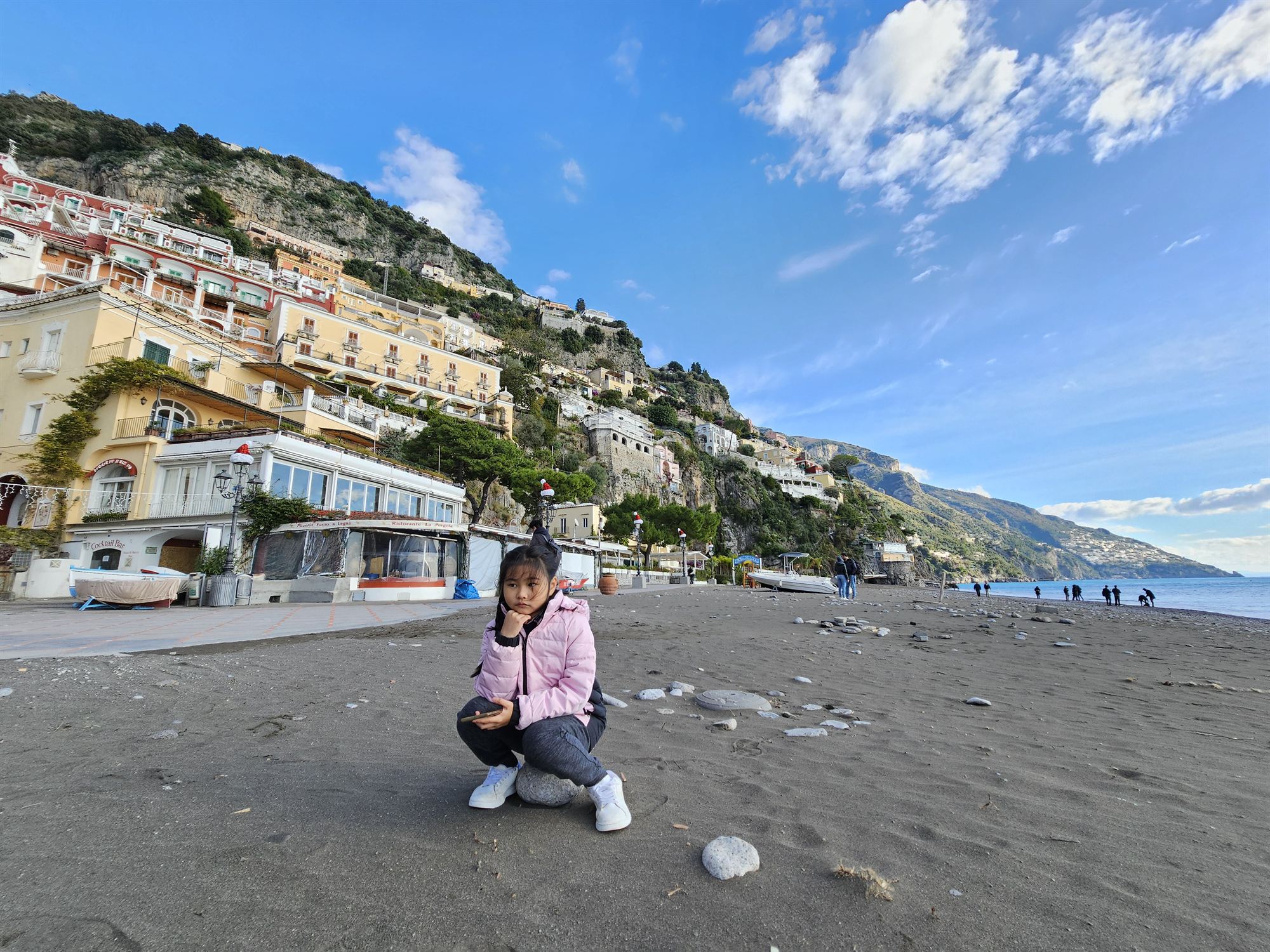 Our daughter crouching on the pebble beach at Positano