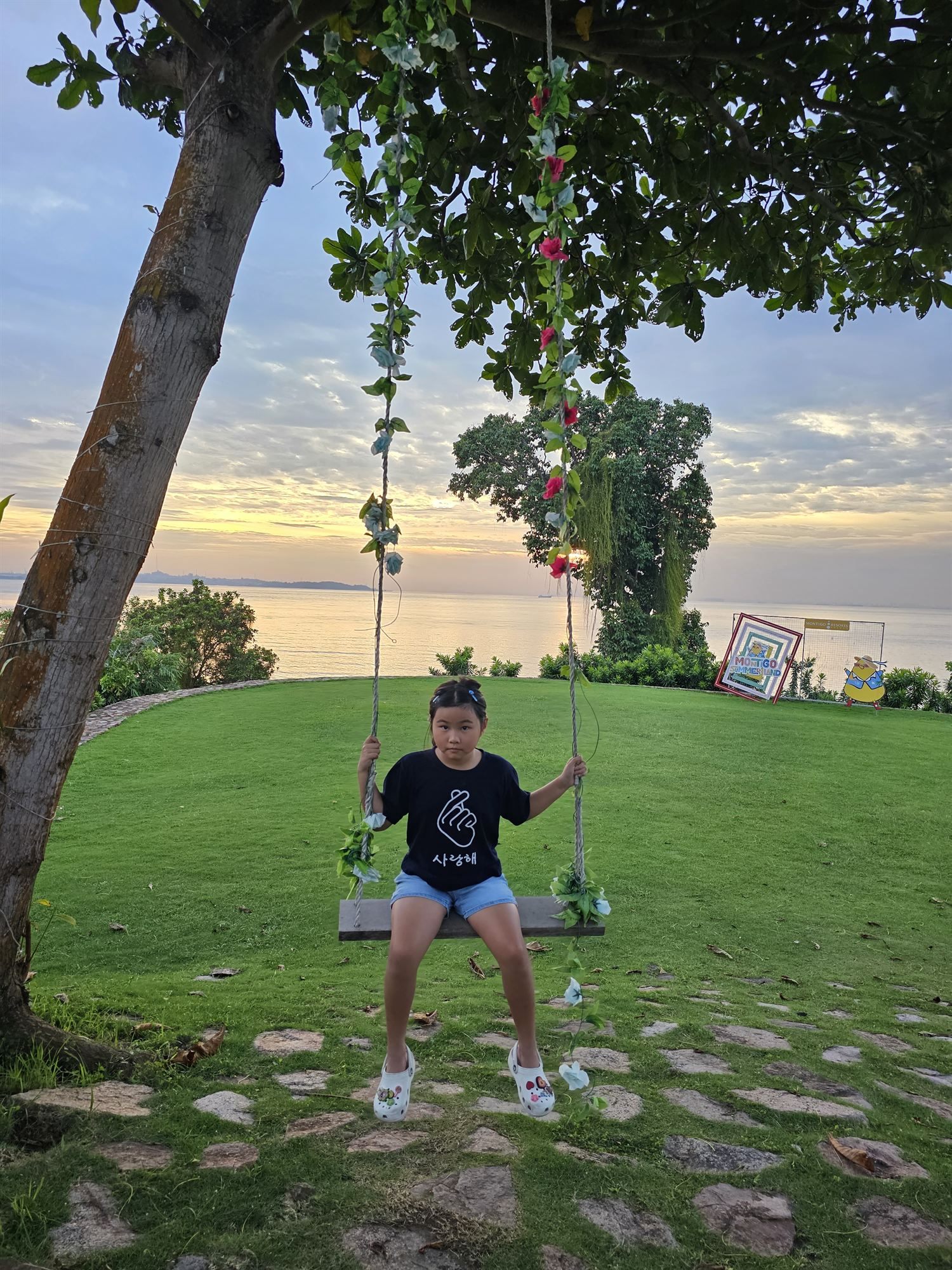 Child on a flower-decorated swing at sunset, Montigo Resort, Batam
