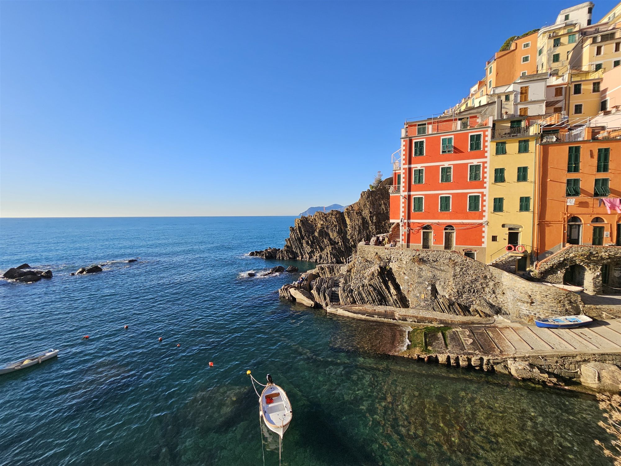 Riomaggiore's harbour from the cliff, a moored white boat in the clear water and the pastel houses above