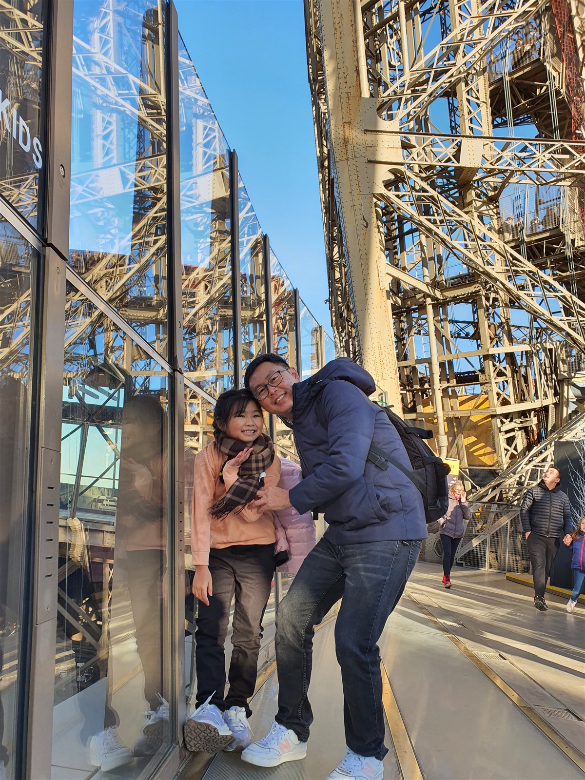 Father and daughter posing beside the glass panels on the Eiffel Tower's first level