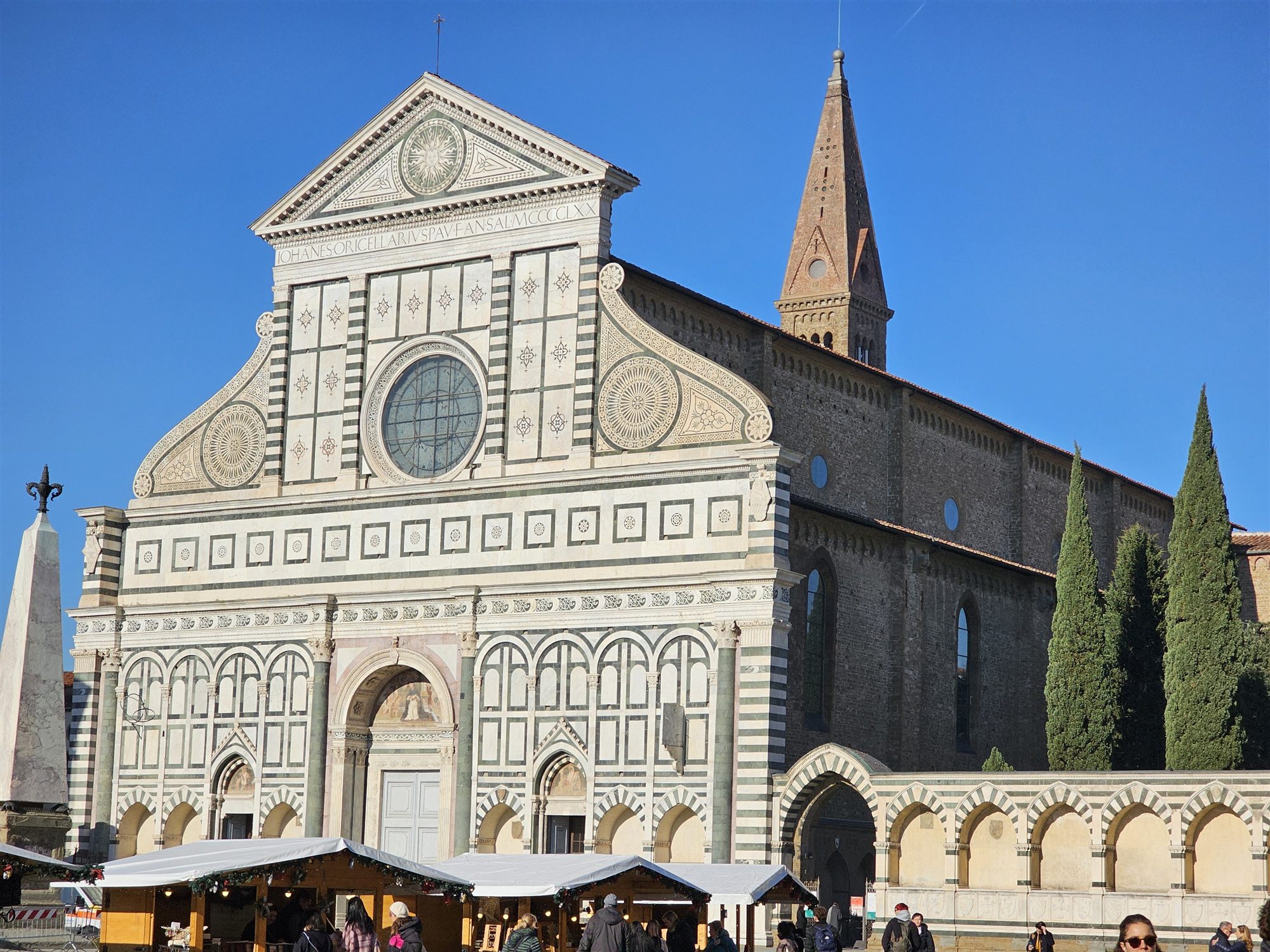 The green and white marble facade of Santa Maria Novella, with a Christmas market in front