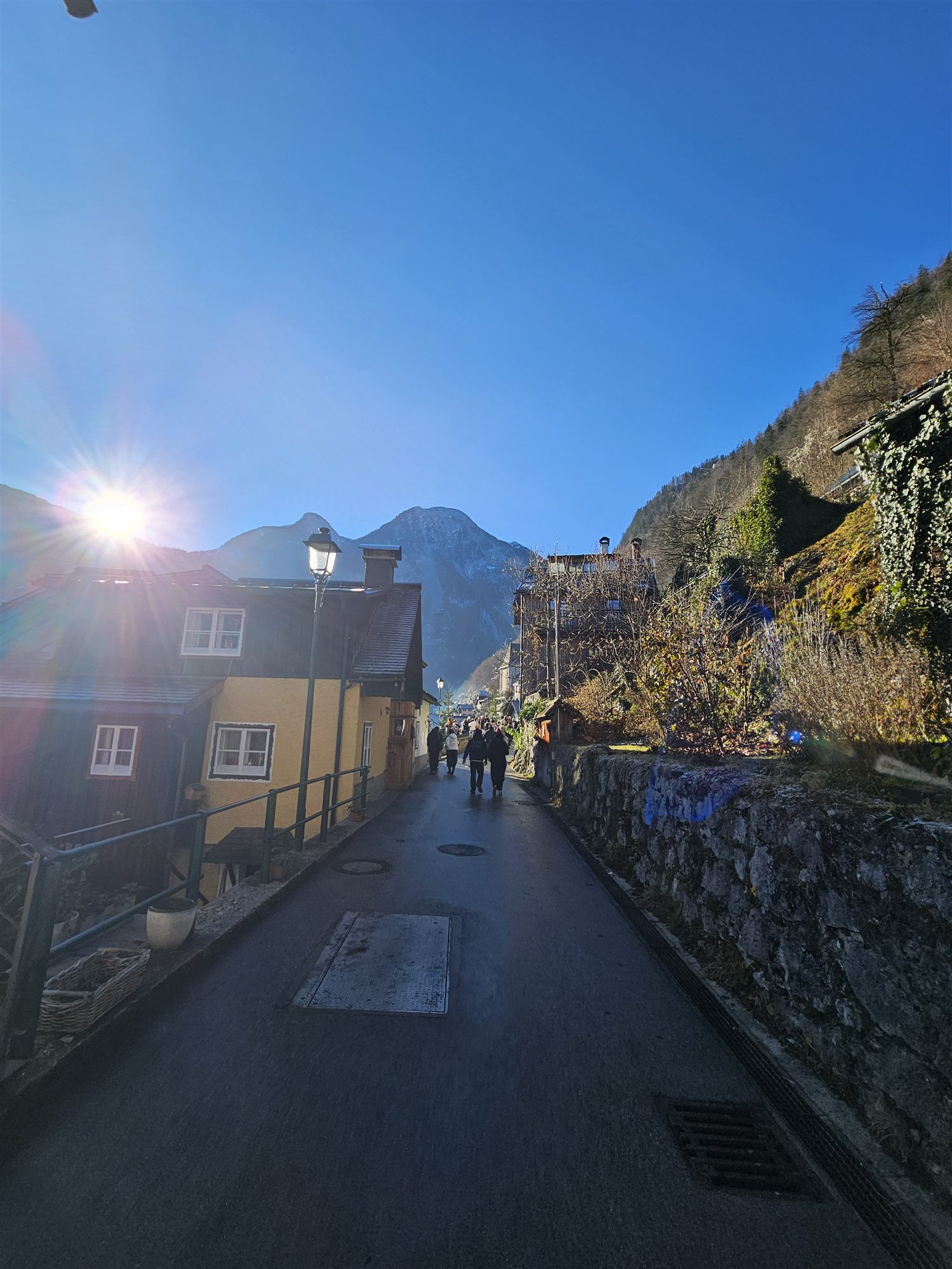 A street in Hallstatt leading downhill toward the lake, sun breaking over the mountains