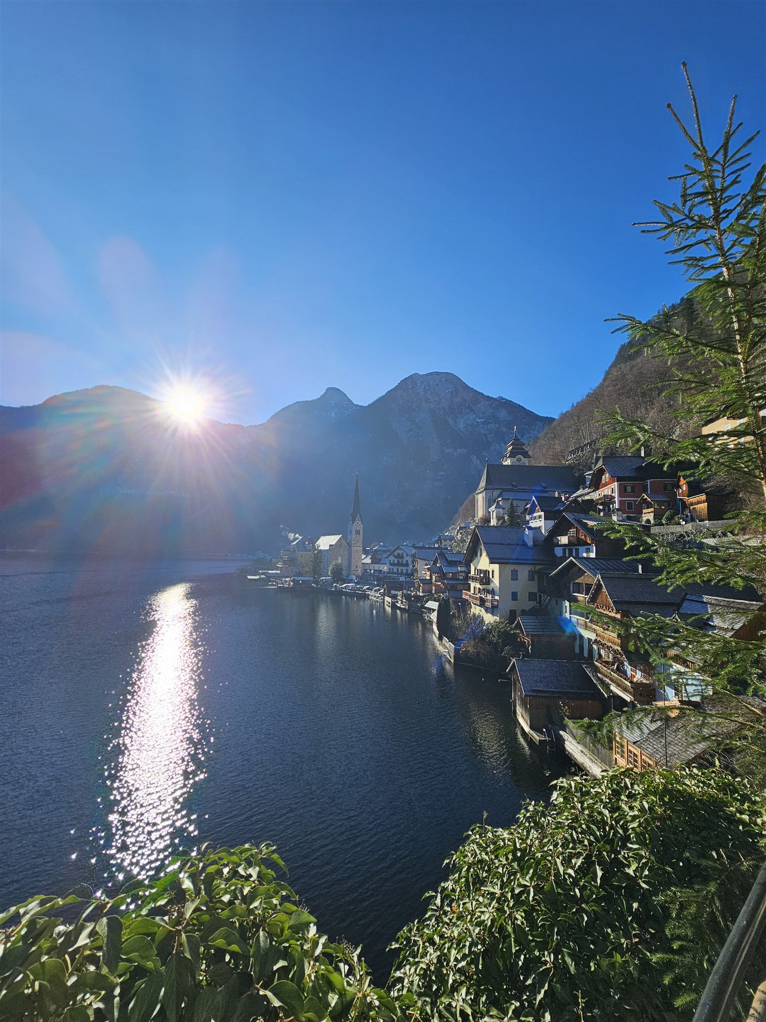 Sunburst over Lake Hallstatt with the village and mountains, sun climbing higher