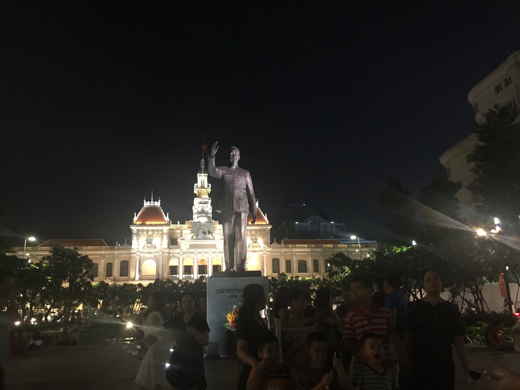 The City Hall building lit up at night, with crowds gathered near the Ho Chi Minh statue