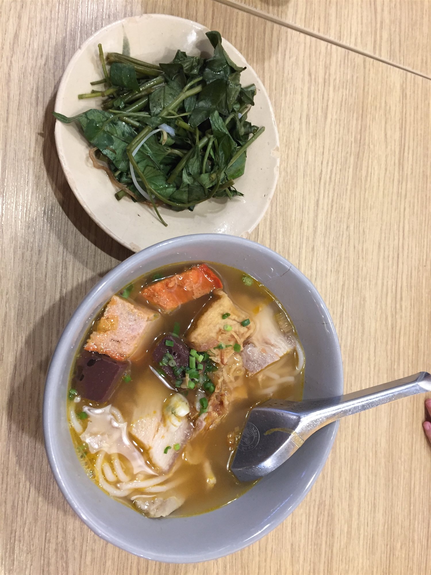 A bowl of Vietnamese noodle soup with a side plate of fresh herbs