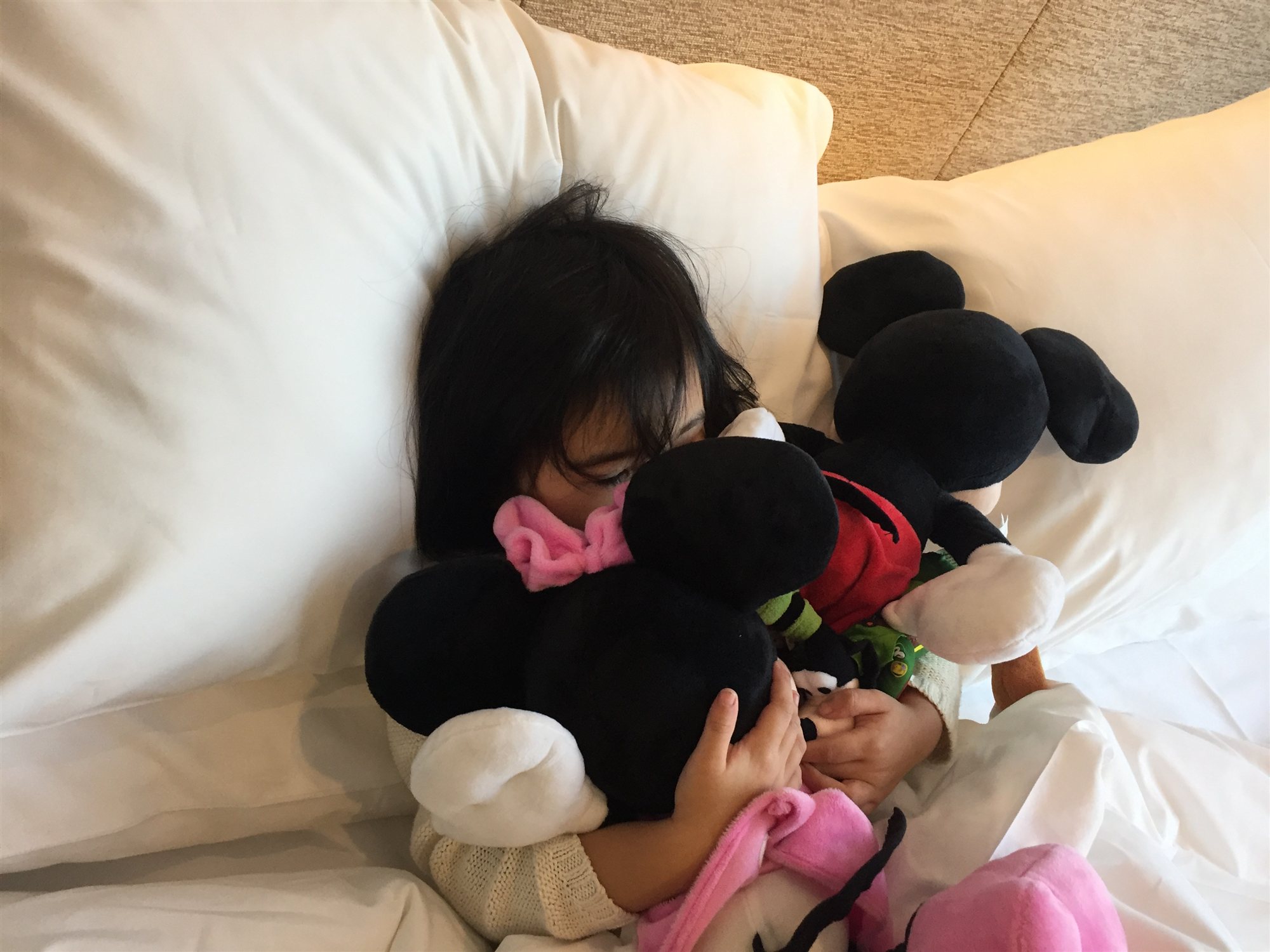 Our daughter asleep in bed, hugging a pile of Mickey and Minnie plush toys