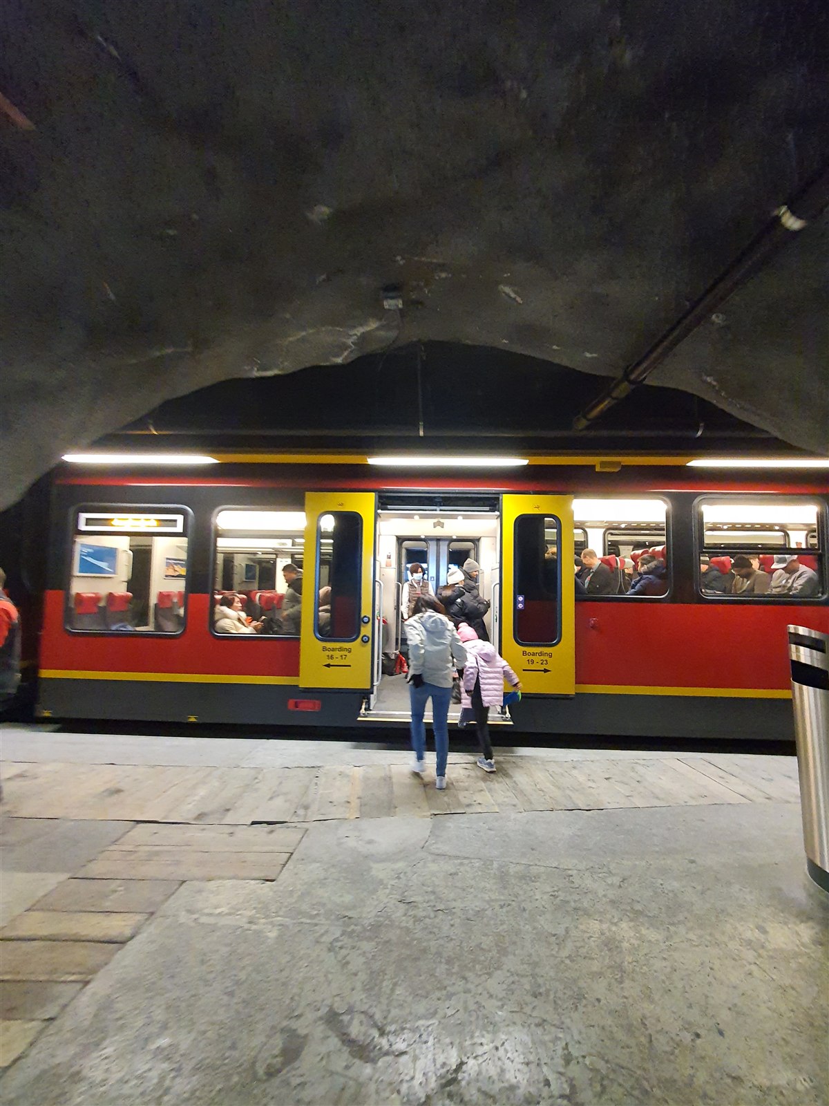 Passengers boarding a red and yellow Jungfrau Railway train at a tunnel platform