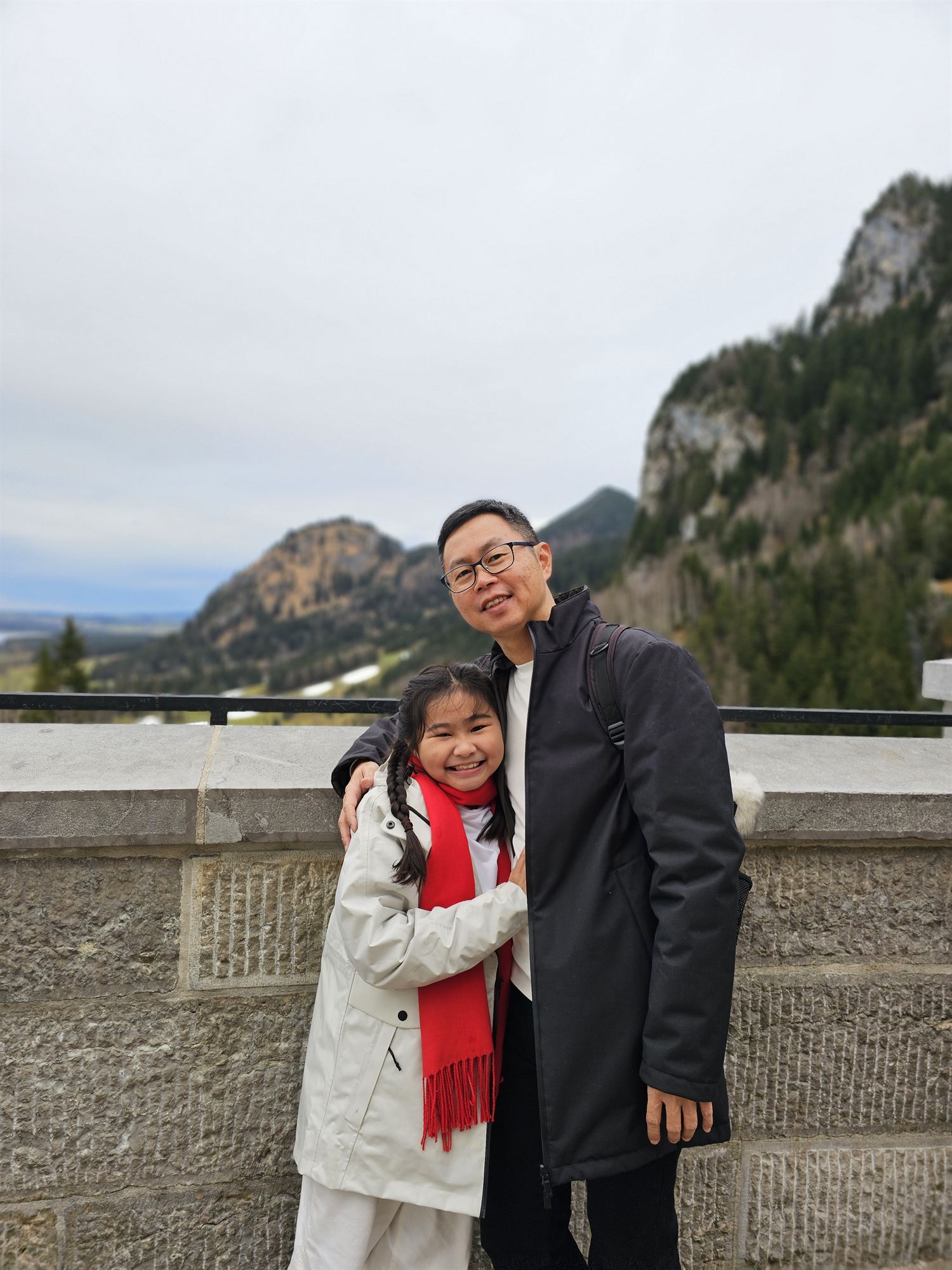 Father and daughter portrait at a viewpoint near Neuschwanstein Castle, mountains behind