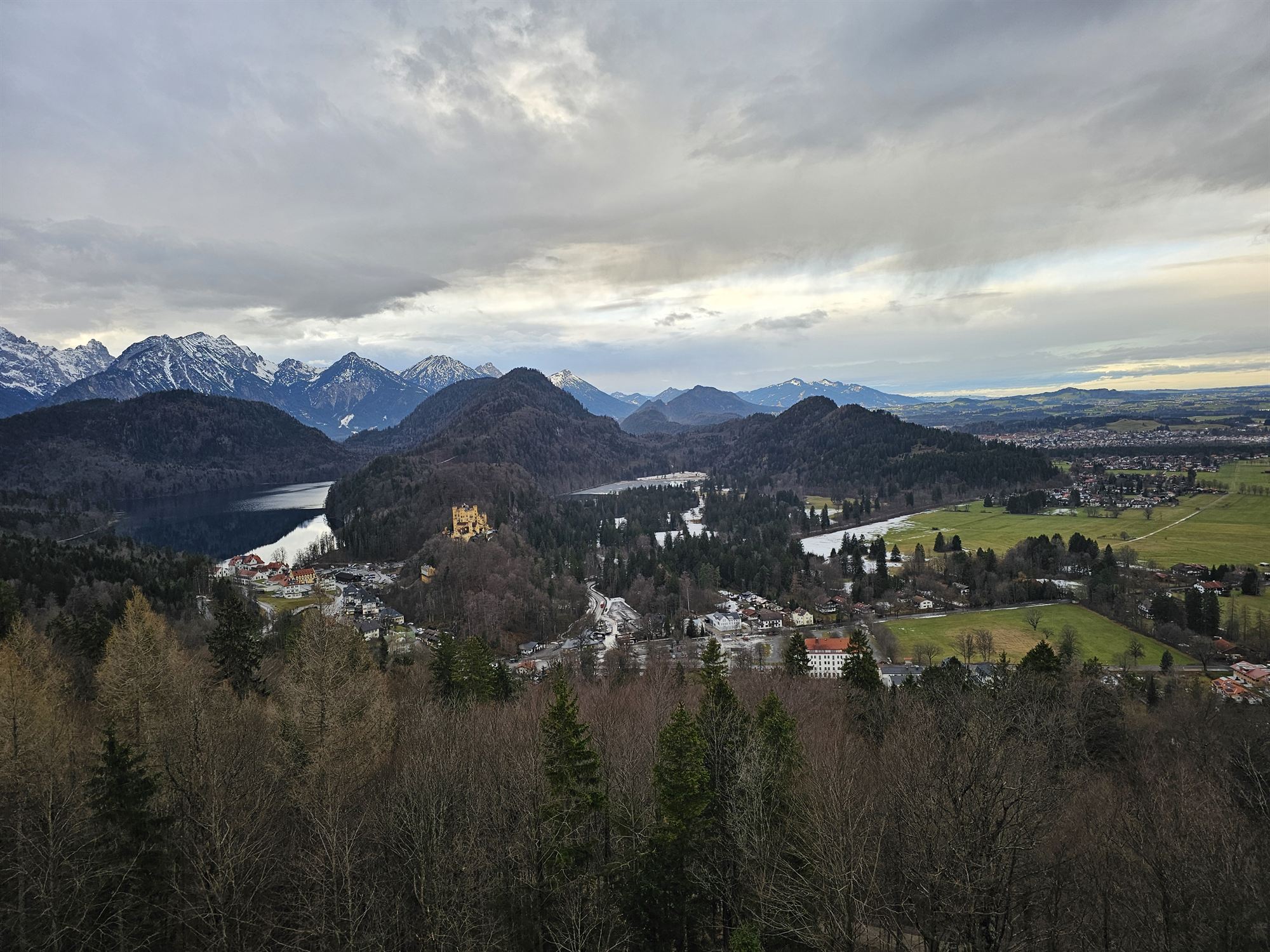 Aerial view of Hohenschwangau Castle, a lake, and the valley below, seen from above Neuschwanstein