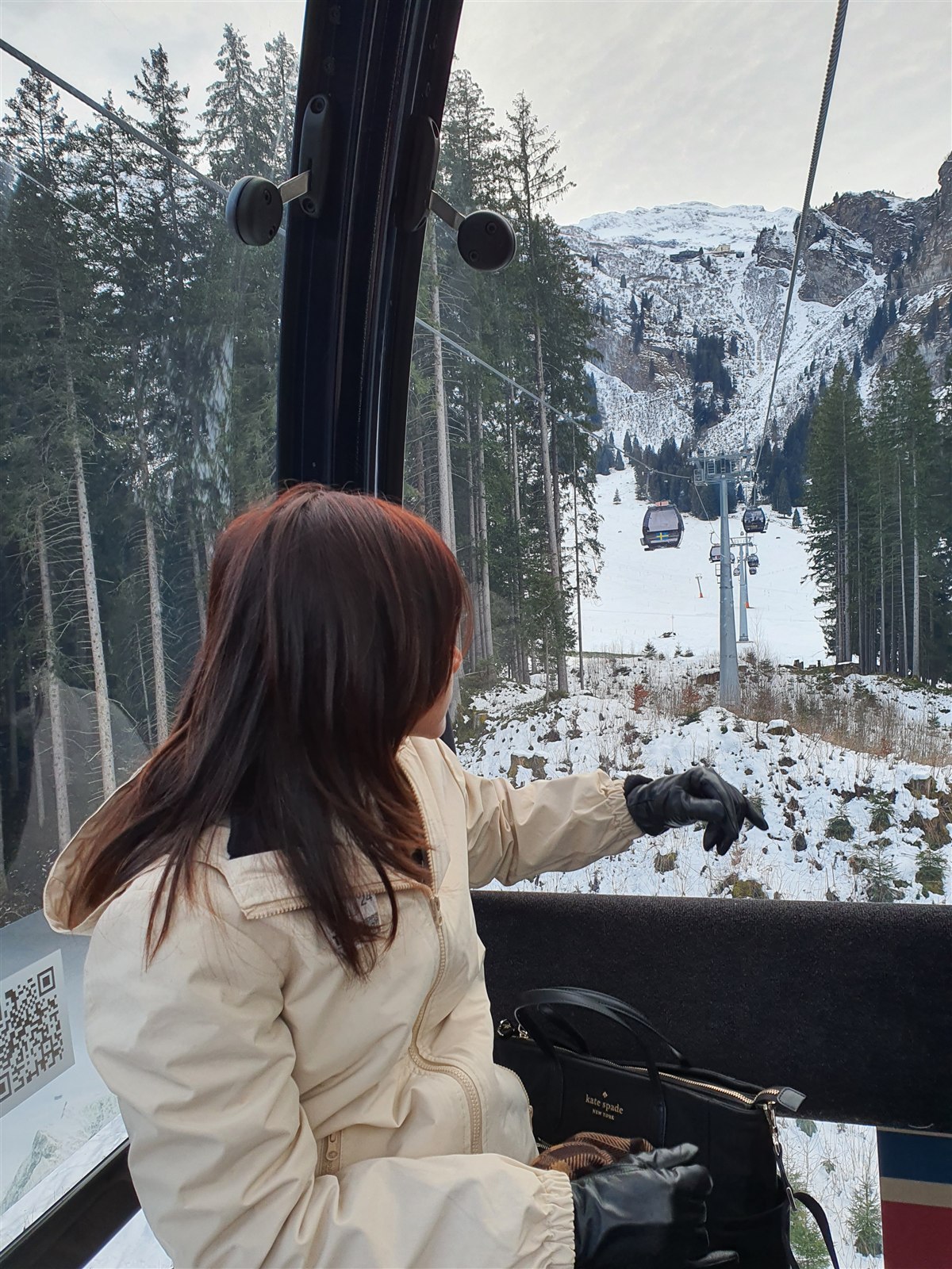A girl pointing out of a cable car window at snowy slopes and cable car lines