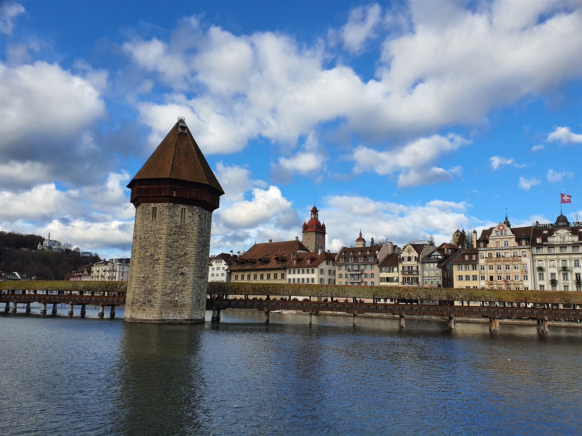 The octagonal Wasserturm beside the covered Kapellbrücke, with old town buildings and the Hotel des Alpes behind