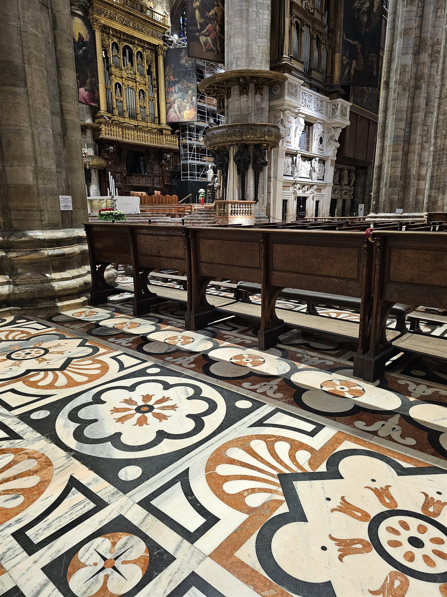 The inlaid marble floor of the Duomo di Milano, with dark wooden pews beside it