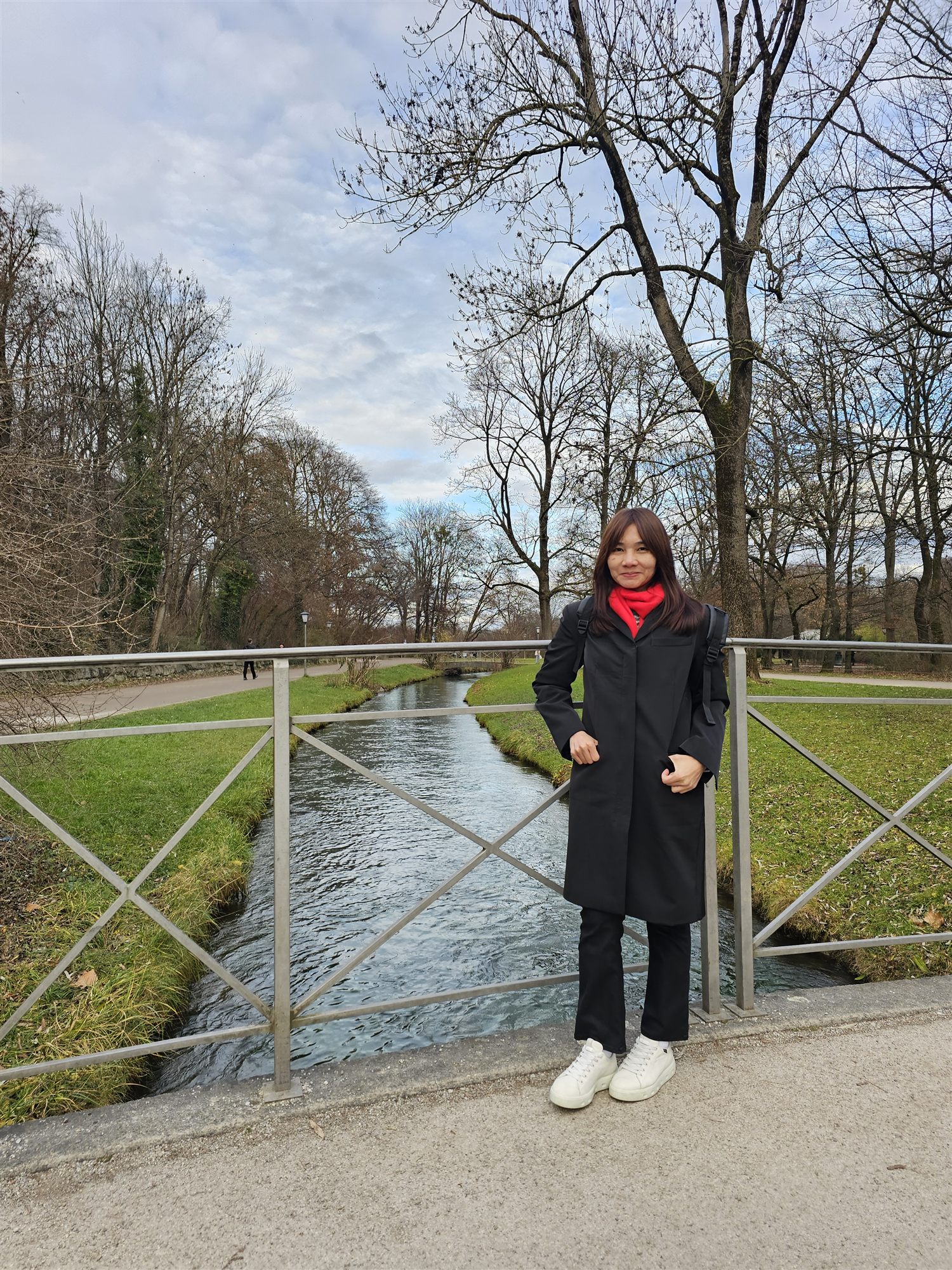 Standing on a bridge over a grassy canal in the English Garden, bare winter trees behind