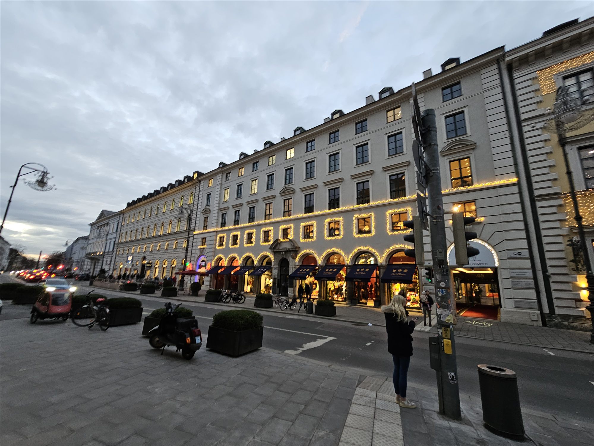 Maximilianstraße at dusk, historic stone facades and shopfronts lit with warm string lights