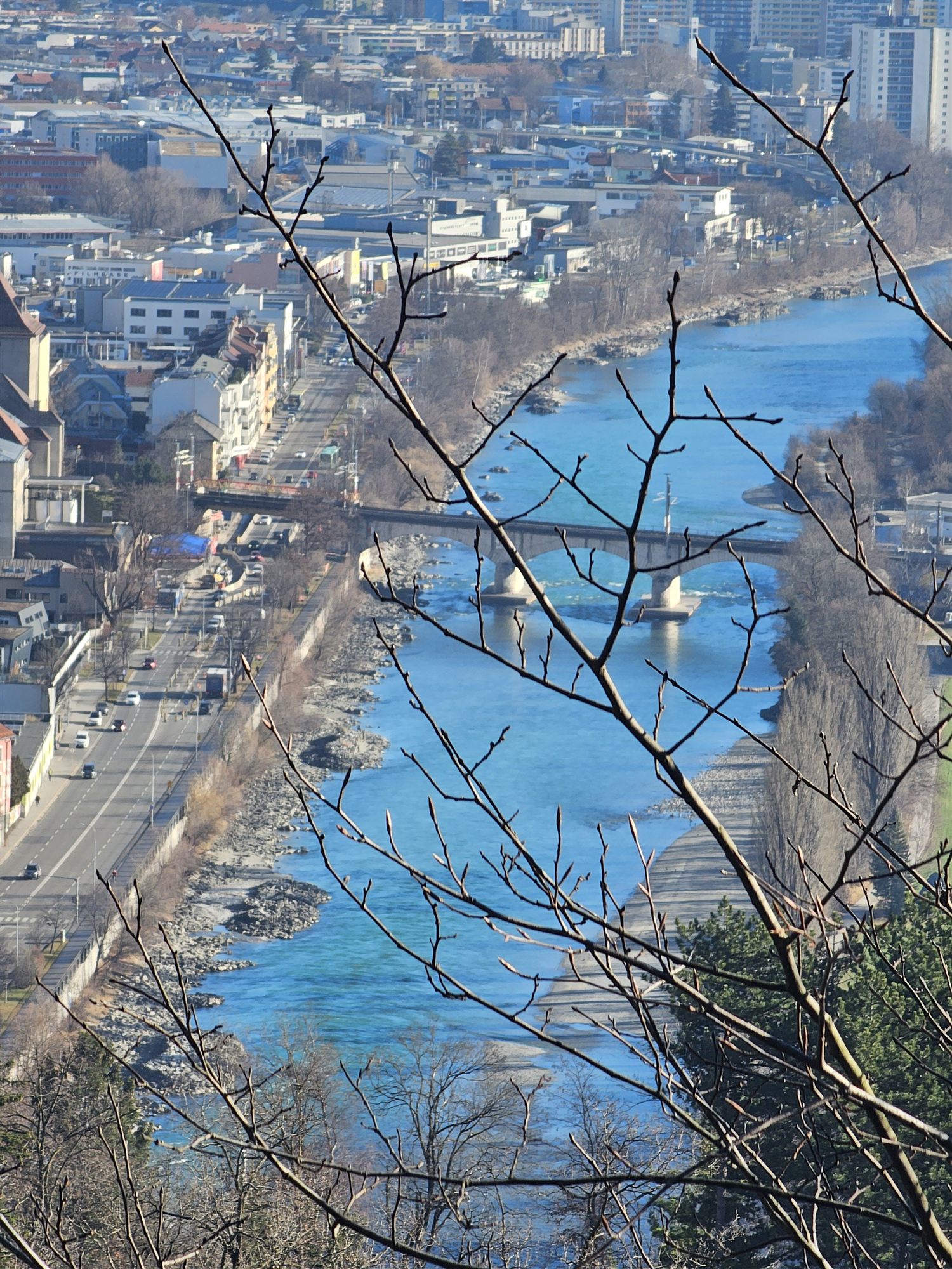 The Inn River and a railway bridge in Innsbruck, seen through bare branches