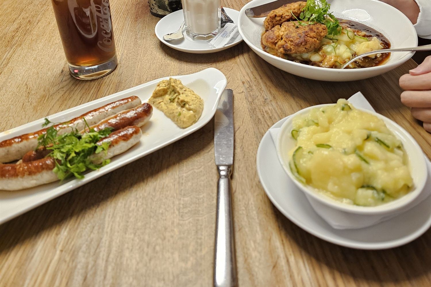 Bavarian lunch on a wooden table near Nymphenburg Palace: grilled sausages with mustard, pork schnitzel in gravy, and creamy potato salad
