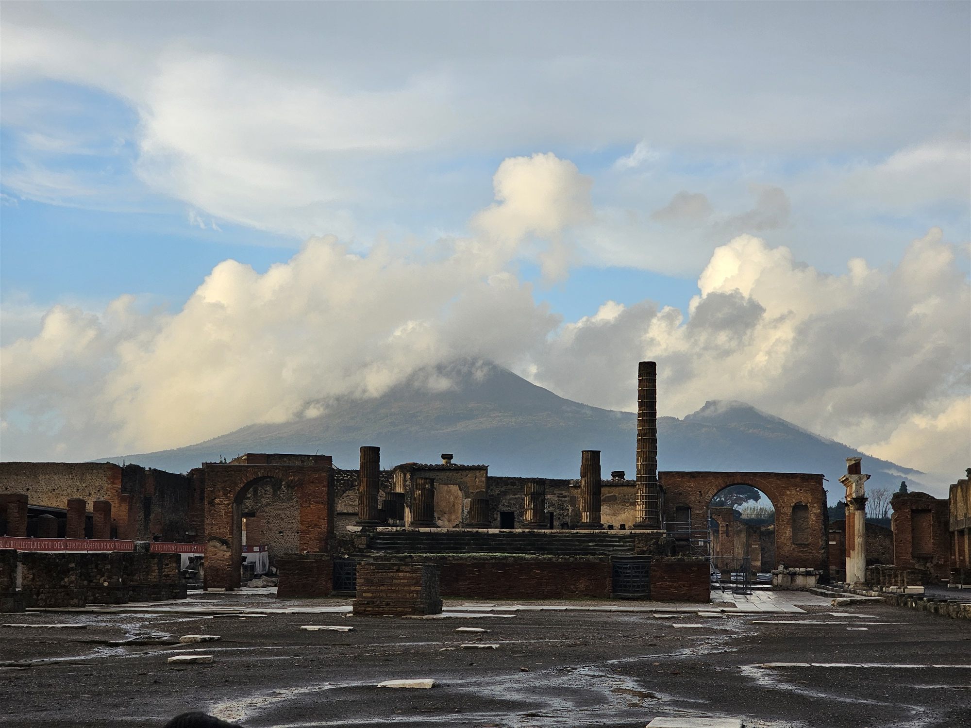 The Forum at Pompeii with the ruins in the foreground and Mount Vesuvius rising behind under clouds