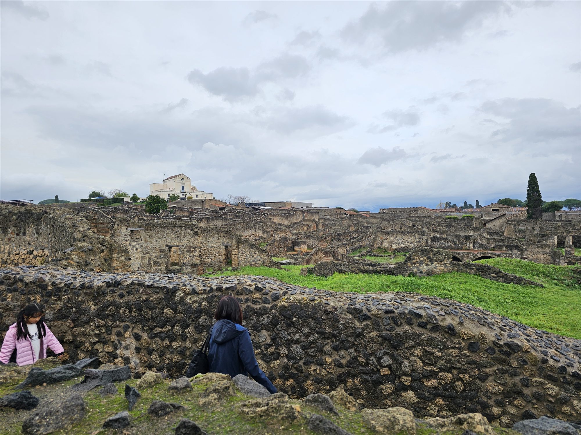 Excavated Pompeii seen from above, a white church on the hill beyond the ruins