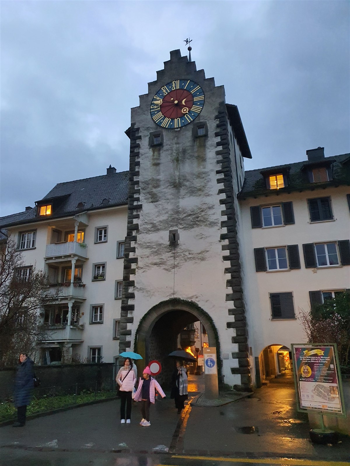 The clock tower of Stein am Rhein's old town gate at dusk, with people walking through the arch