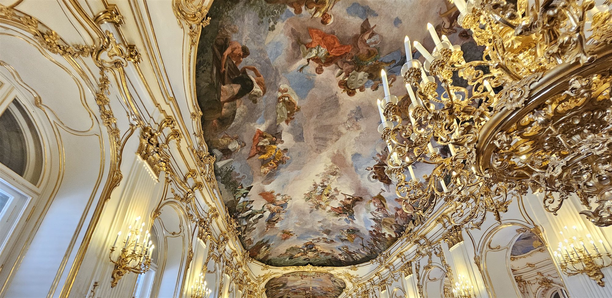 The Great Gallery at Sch&ouml;nbrunn Palace, gilded walls and a frescoed ceiling, visitors walking its length