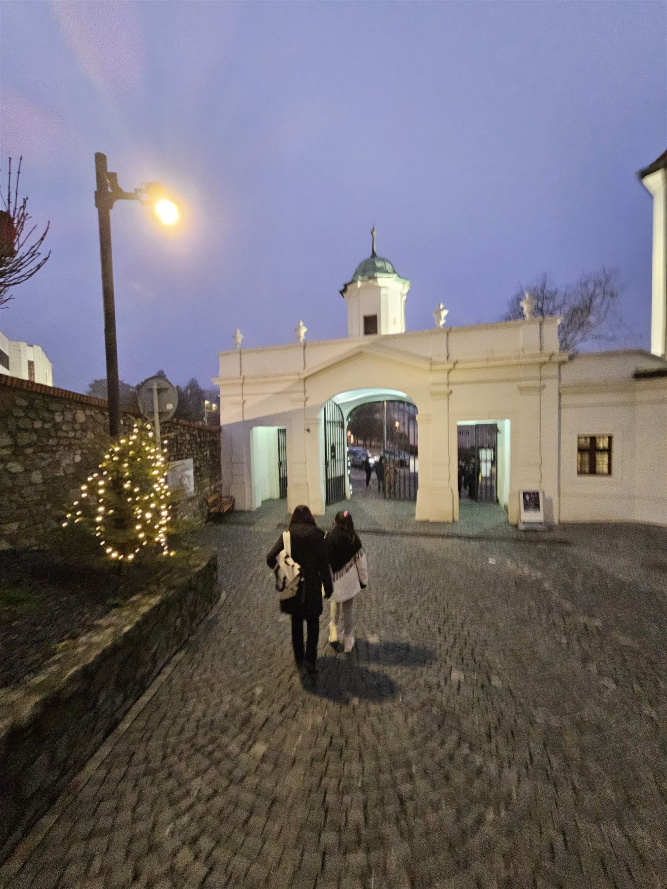 Bratislava Castle's gatehouse at blue hour, with a lit Christmas tree beside the path