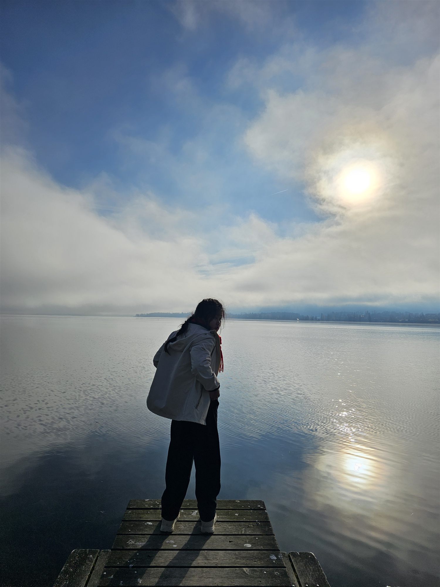 A silhouette on the jetty at Mondsee, sun breaking through the fog over the lake