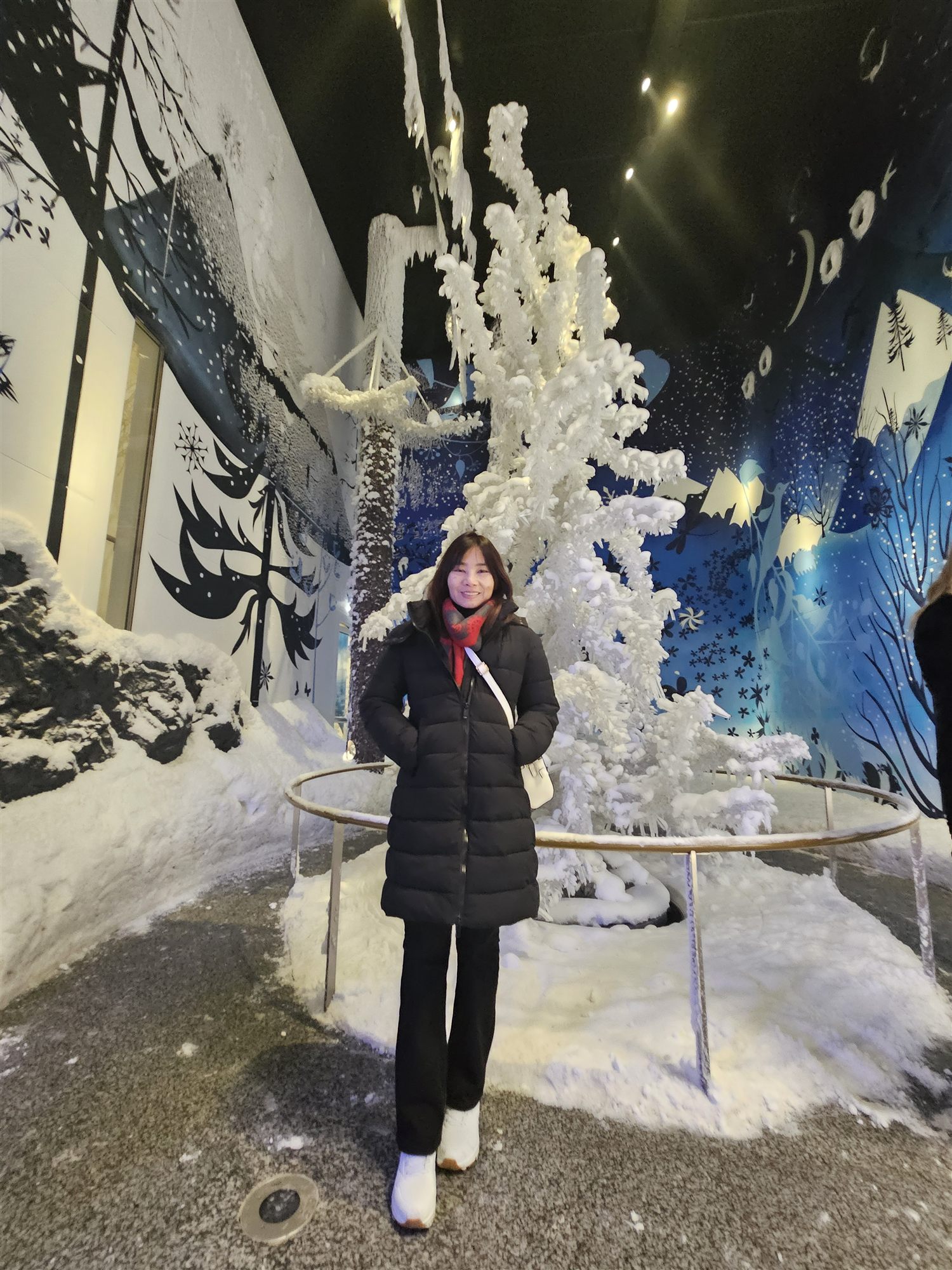 A frosted winter tree installation at Swarovski Crystal Worlds, illustrated mural behind