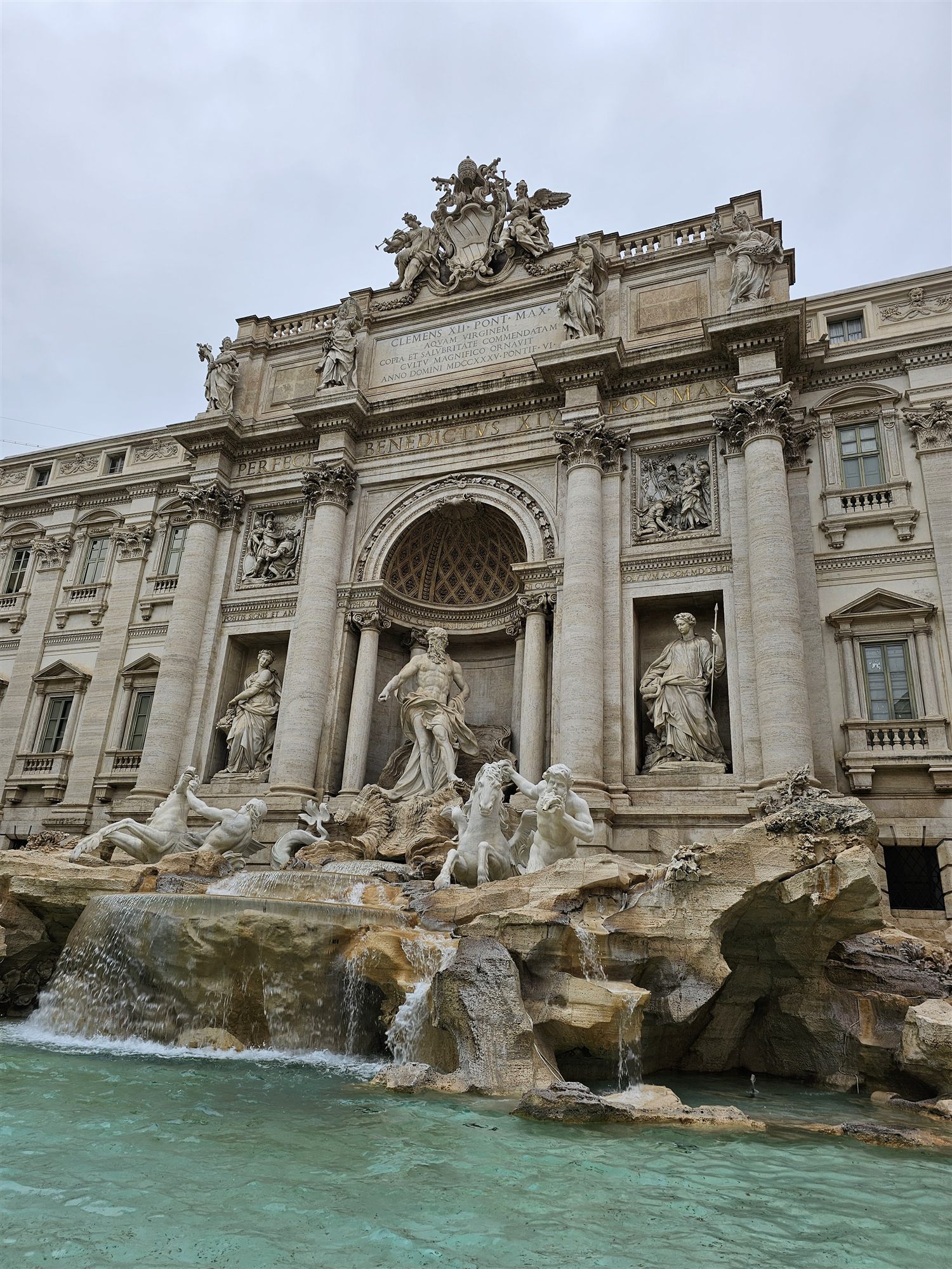 The Trevi Fountain's baroque facade and Oceanus statue, seen from the square on an overcast day