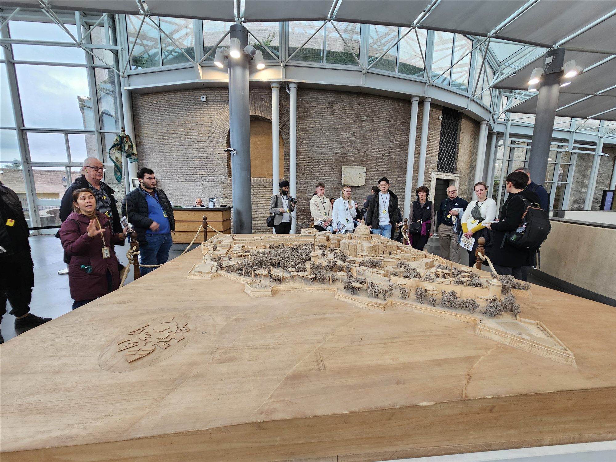 A carved wooden scale model of Vatican City and St Peter's Basilica, with a guide explaining it to a tour group