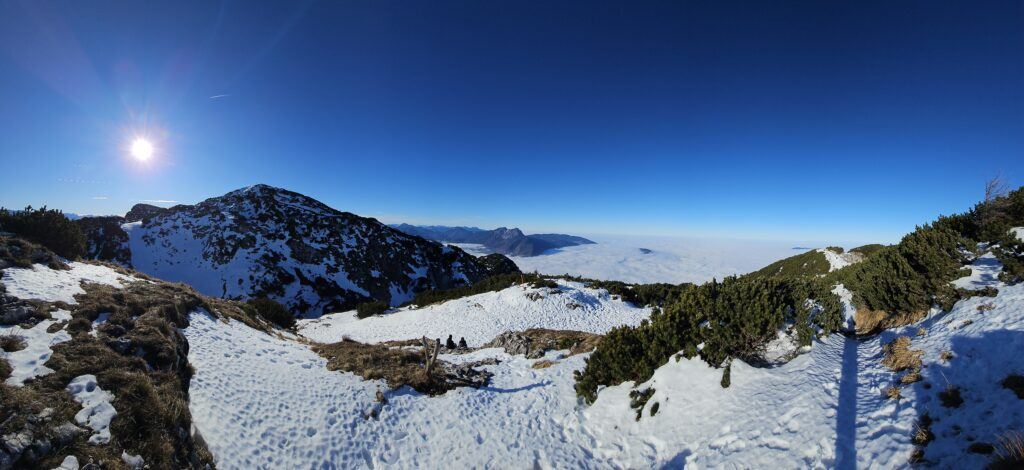Panoramic view from Untersberg summit over a sea of clouds, sun flaring over the ridge