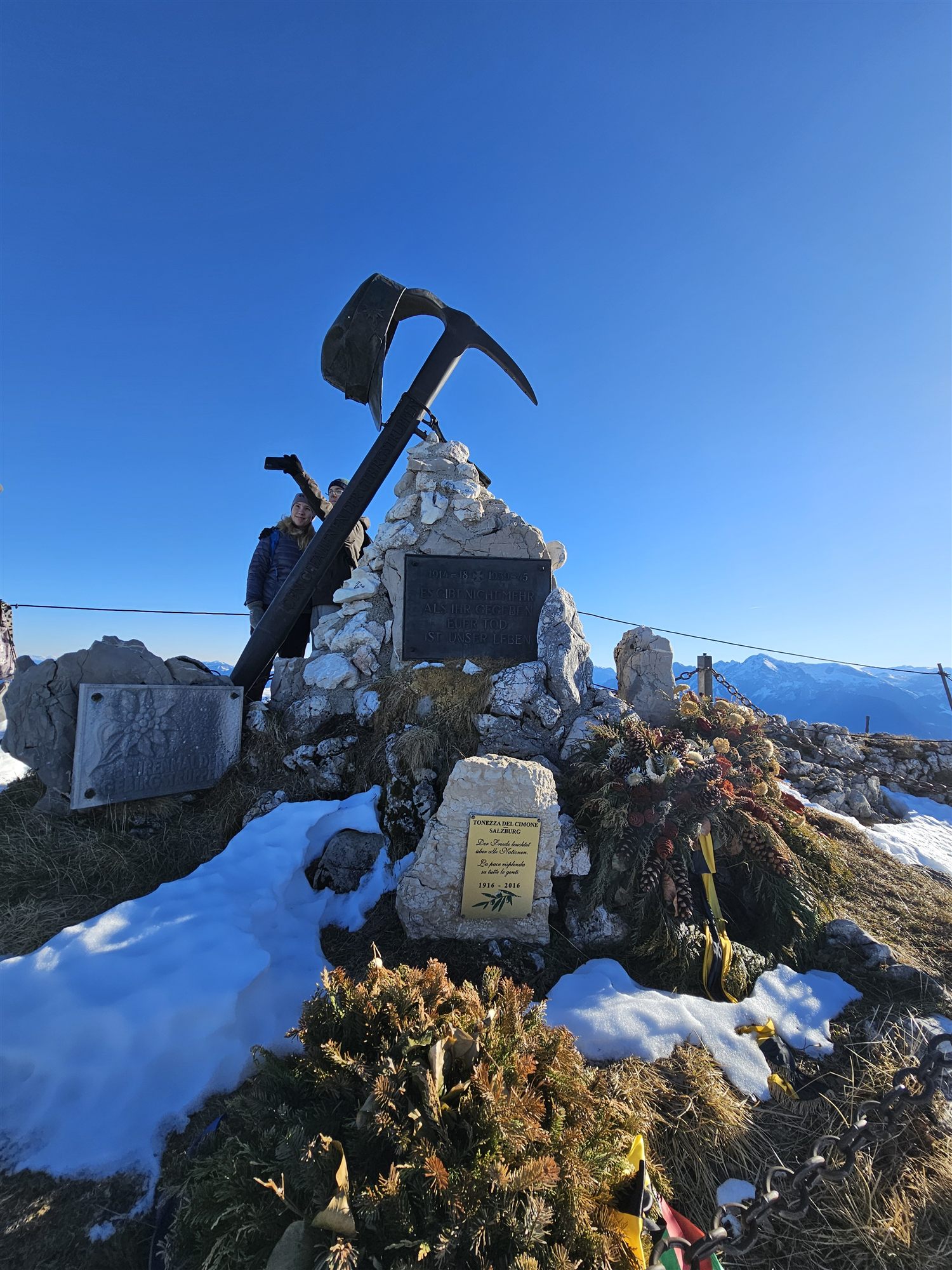 War memorial cairn topped with an ice axe at the Untersberg summit, with commemorative plaques