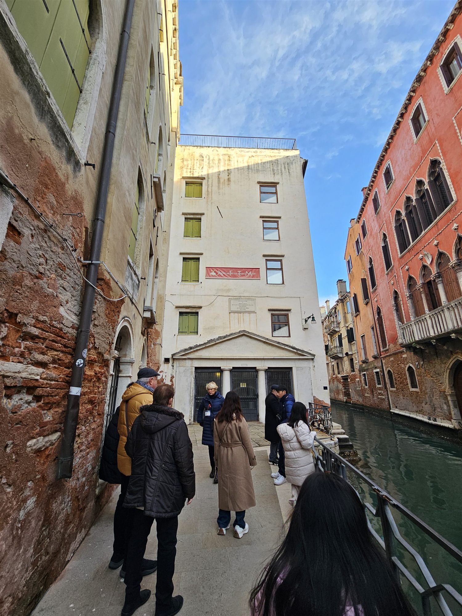 Our walking tour group following the guide along a narrow Venice alley toward a white theatre facade