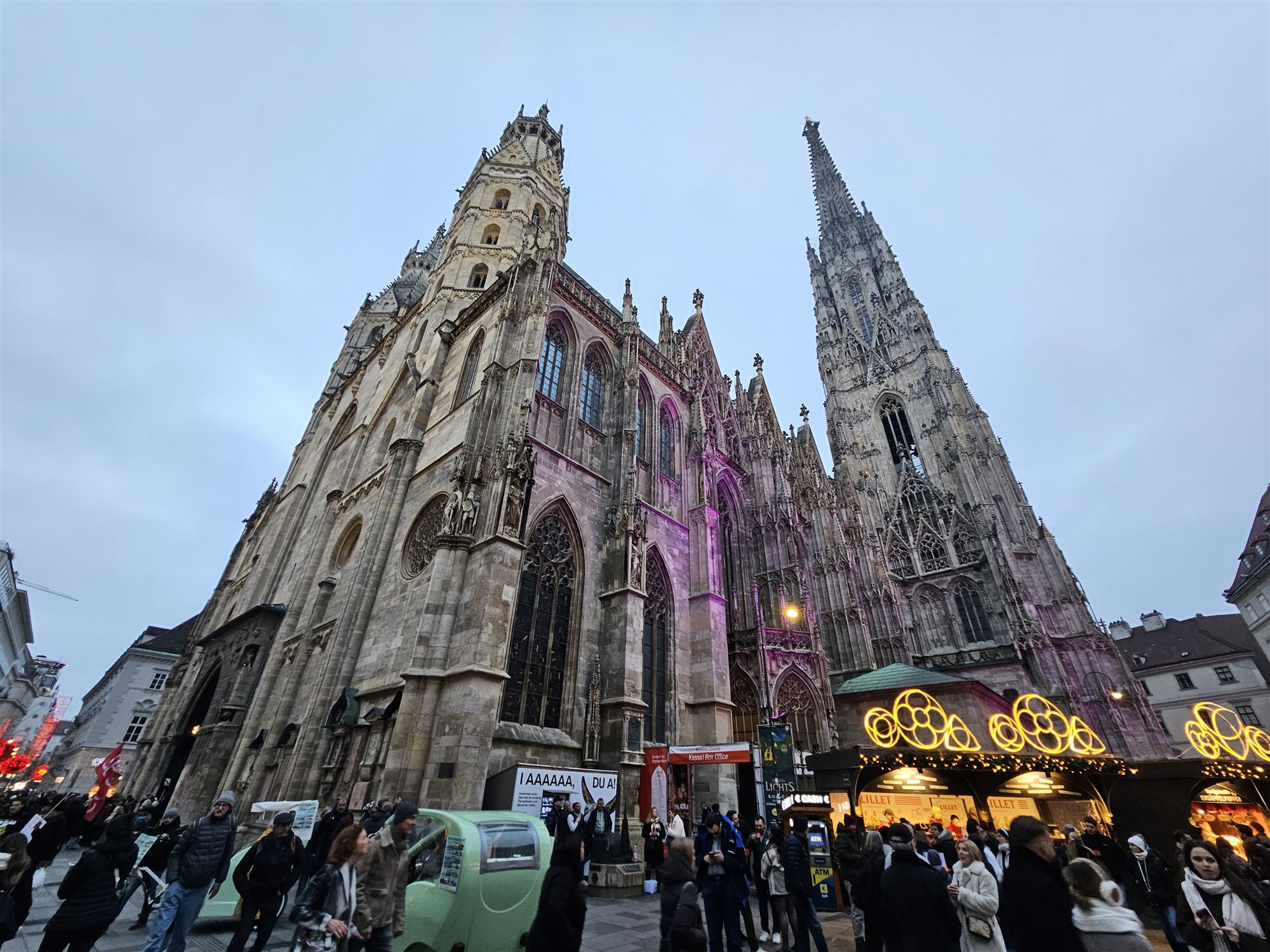 St. Stephen's Cathedral lit in purple at dusk, with Christmas market stalls in front