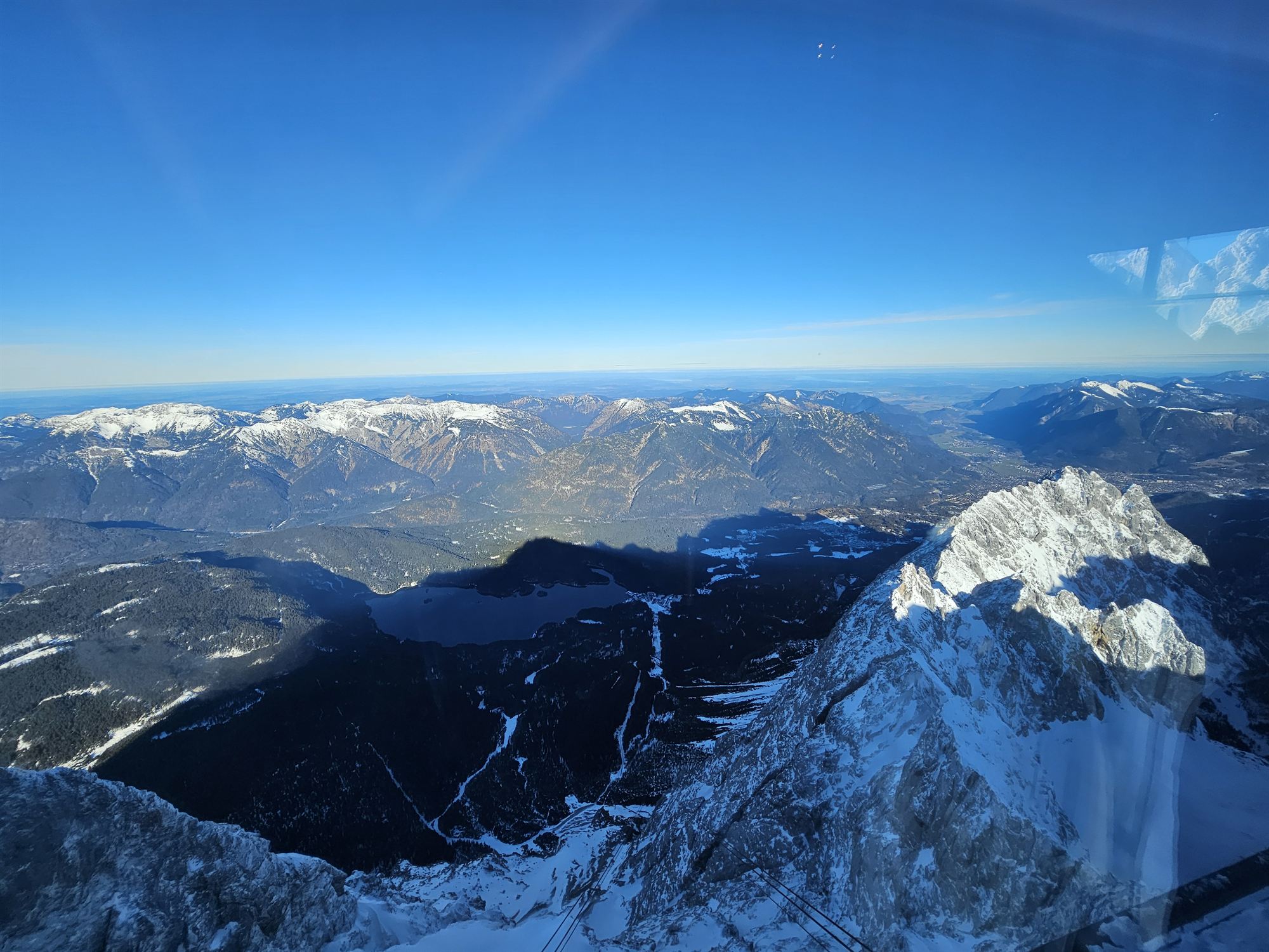 View from the cable car window of a frozen lake and mountain ridges below Zugspitze