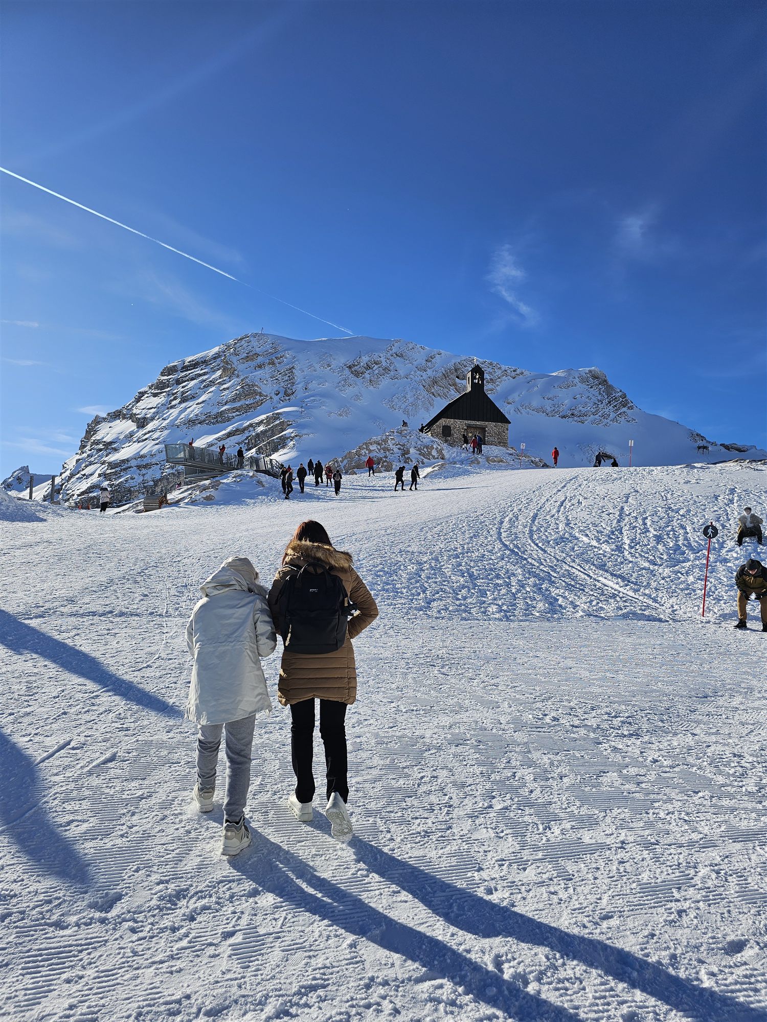 Two visitors walking across the snowy plateau toward the Zugspitze chapel