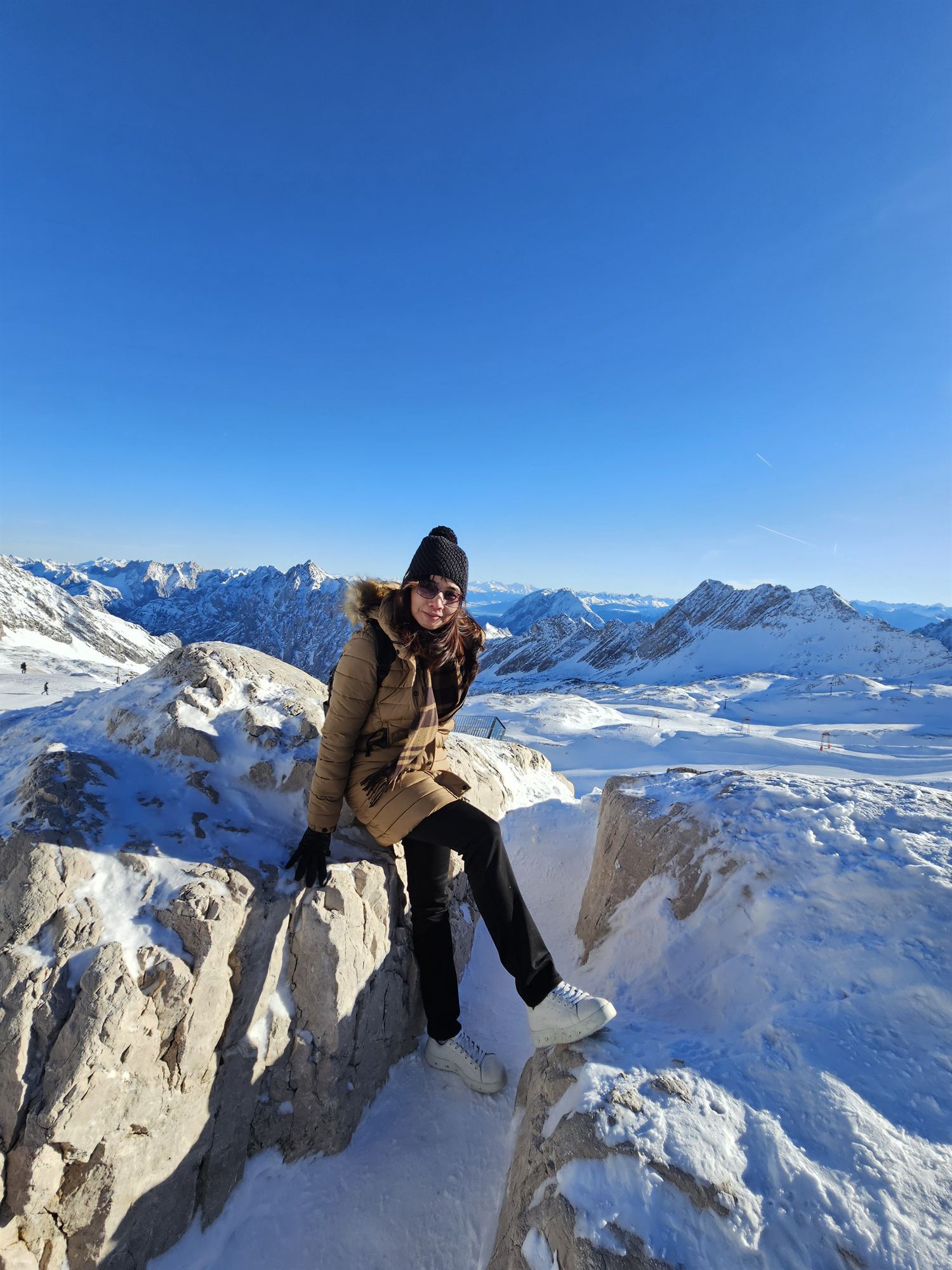 Sitting on an exposed summit rock ledge at Zugspitze, mountains stretching to the horizon